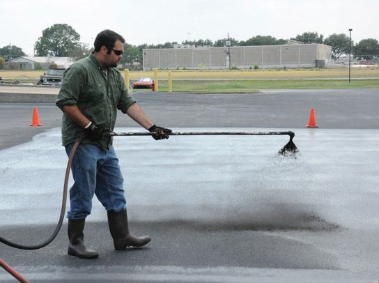 A professional applicator applies coal-tar-based sealcoat to a test plot used to measure emission of polycyclic aromatic carbons (PAHs) into the air