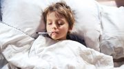 Child Sick in Bed With Thermometer