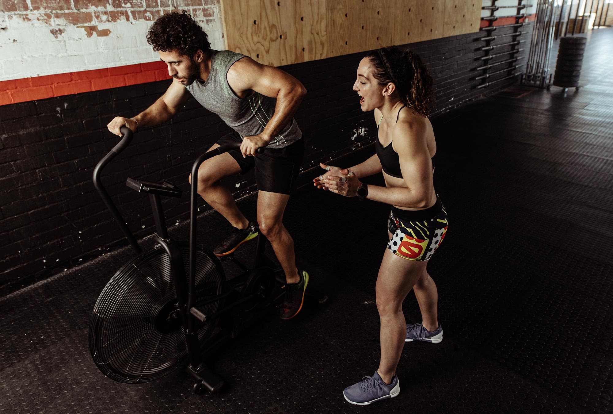  A man and woman are exercising in a gym. The man is on an exercise bike and the woman is standing next to him, clapping and cheering him on. The image represents the search query 'Tips for maintaining motivation in exercise'.