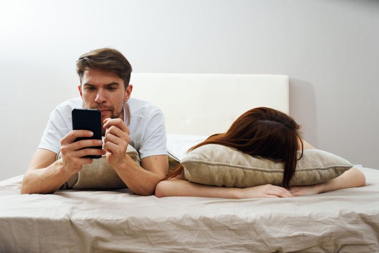 Man Checking Phone Woman Sleeping Bed